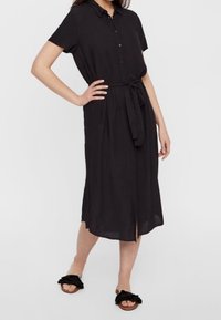 Black, short-sleeve dress with a button front, belted waist, and knee-length, featuring a soft, smooth fabric and a slit at the front.