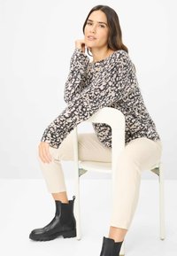 Striktrøje i beige og sort leopardmønster, rund halsudskæring, afslappet pasform, parret med cremefarvede fløjl bukser og sorte ankelstøvler.