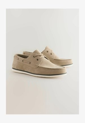 Beige Wildleder-Bootsschuh mit strukturierten Akzenten, flacher weißer Sohle und grauem Gumm trim. Verfügt über dekorative Schnürsenkel und atmungsaktive Perforationen.