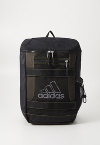Svart ryggsäck med texturerad tyg, nätfickor på sidan, flera fickor med dragkedja och en framträdande vit Adidas-logotyp med gröna detaljer.