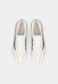 Ζεύγος λευκών ποδοσφαιρικών παπουτσιών με μαύρες ρίγες, κόκκινες λεπτομέρειες και τη λέξη "COPA" τυπωμένη στο εσωτερικό, οπτική από πάνω σε λευκό φόντο.