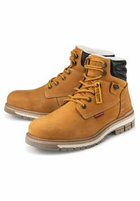 Bruine leren enkellaarzen met zwarte accenten, gewatteerde kraag, witte rubberen zool en gele veters. Bevat logo-labels aan de zijkant.