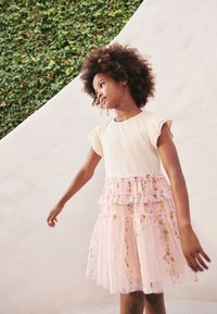 Lichtbeige top met korte volantmouwen, gelaagde roze rok met bloemmotieven en glitters. Zachte, vloeiende stof.