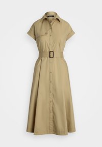 A knee-length, tan shirt dress features a button-down front, short rolled sleeves, and a coordinating belt at the waist.