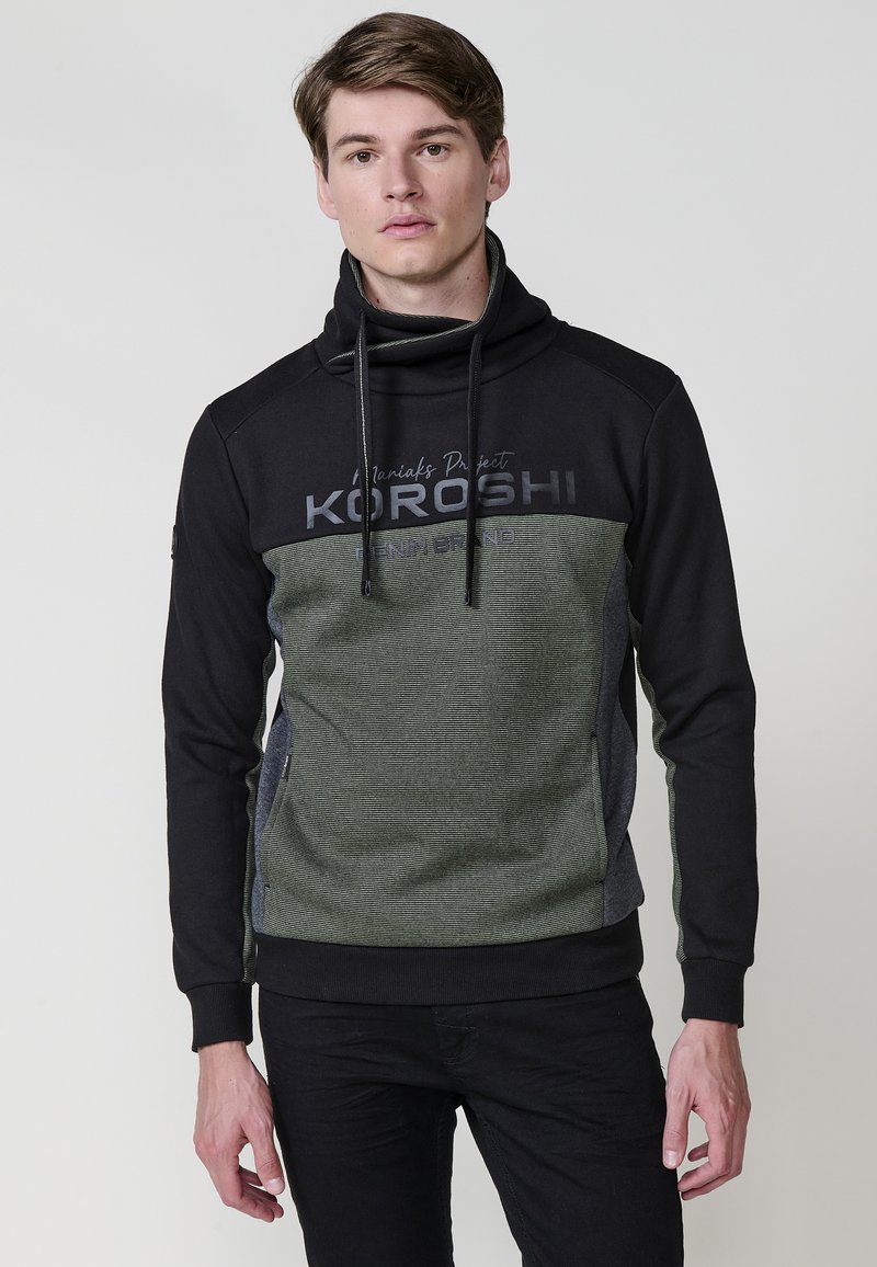 Sudadera con capucha en negro y verde. Presenta un diseño texturizado a rayas y letras en negrita. Incluye cordones y puños de canalé.