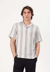 Camisa de manga corta, con botones, que presenta un tejido beige claro con rayas verticales gris oscuro y un corte relajado.