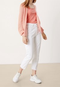 Jasnoróżowy sweter z dzianiny, koralowy top, białe dżinsy sięgające do kostek z postrzępionym dołem oraz białe sneakersy. Swobodny zestaw z warstwową teksturą.