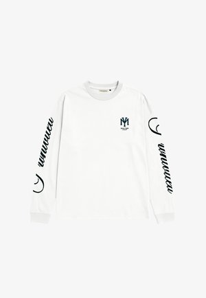 Valge pika varrukaga särk, mille mõlemal varrukal on musta kirjatööga tekst ja rinnal väike must logo, millel on tähed „NY“ ja „Modern Yuppies“.