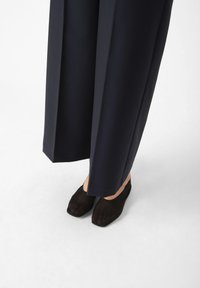 Pantaloni blu con design a gamba larga, caratterizzati da una trama liscia. Scarpe nere slip-on con punta affusolata e tomaia semi-trasparente.
