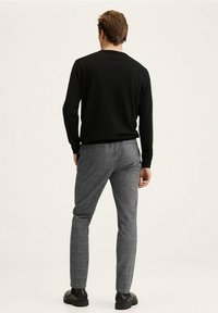 Zwarte gebreide trui met ronde hals, gecombineerd met grijs geruite broek. De outfit wordt compleet gemaakt met stijlvolle zwarte schoenen.