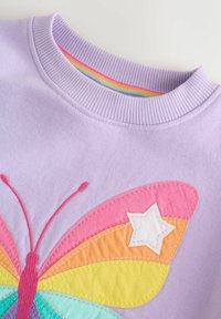 Lila dukserica s velikim dizajnom leptira s višebojnim krilima u ružičastoj, narančastoj i tirkiznoj boji, uz bijeli zvjezdani naglasak.