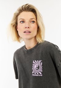 Donkergrijze T-shirt van katoen met een ronde hals. Beschikt over een roze spiraal graphic en de tekst "PROTEST & CO" op de linkerkant van de borst.