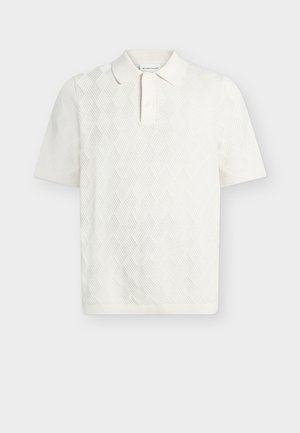 Polo blanc à manches courtes avec motif texturé en losanges et col à patte à deux boutons.