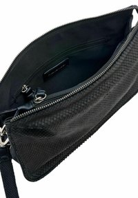 Pochette noire texturée avec fermeture éclair ouverte, montrant un intérieur doublé avec une petite poche zippée et une bandoulière détachable.