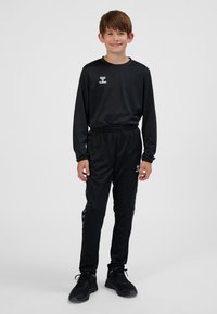 Czarny sportowy dres z długimi rękawami i elastycznym pasem, z logo na piersi oraz akcentami w kształcie jodełki po bokach spodni.