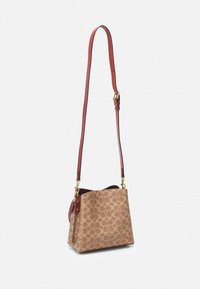 Brown patterned handbag with a smooth texture and a structured shape. Features a detachable red leather strap and gold hardware accents.
