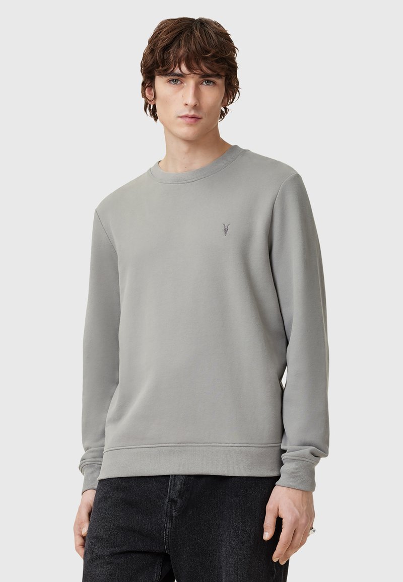 Sudadera gris de cuello redondo en una tela suave, con mangas largas y un sutil logo bordado en el pecho. Corte estándar.