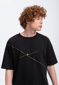 T-shirt en coton noir avec un design minimaliste présentant un graphique d'une figure en équilibre sur deux lignes qui s'intersectent, ajoutant une touche créative.