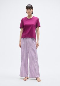 T-shirt à manches courtes fuchsia associé à un pantalon large rayé en violet clair et blanc. Le tissu semble doux avec une coupe décontractée.