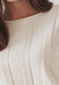 Top a maglia beige chiaro con scollo rotondo rilassato, caratterizzato da una texture a righe verticali e un tessuto morbido e liscio per un'eleganza sottile.