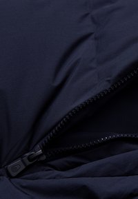Tela de color azul marino con una textura suave que presenta un zipper parcialmente abierto. El zipper tiene un tirador de plástico negro y dientes visibles.