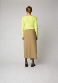 Neon zöld, hosszú ujjú top bézs midi szoknyával párosítva, sima textúrával. Az outfit barna, magassarkú cipőkkel egészül ki.