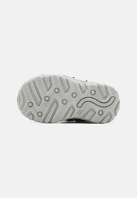 Gummisåle med teksturert, gripende mønster, i lys grå farge med bølgete design og små hevede prikker for bedre grep.