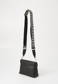Černá kožená kabelka přes rameno se strukturovaným tvarem, s texturovaným povrchem a vzorovaným nastavitelným popruhem černobílé barvy.