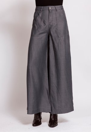 Wide-leg gray pants with front patch pockets worn with black heeled boots and a black top against a light background.