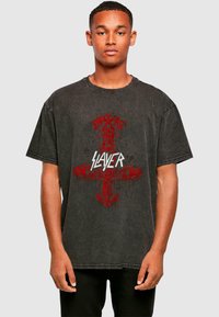 Camiseta gráfica negra con un diseño desgastado, elementos rojos y el texto "SLAYER" en blanco, de manga corta y un corte relajado.