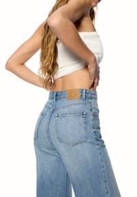 Korkeavyötäröiset vaaleansiniset farkut, joissa on tekstuuri pinta, takana ruskea nahkapatche ja perinteinen viisi taskua -muotoilu.