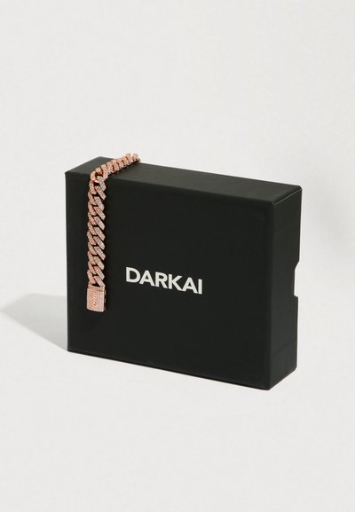 Řetěz s kubánským zapínáním v barvě růžového zlata s vloženými krystaly položený na černé krabici s logem DARKAI na bílém pozadí.
