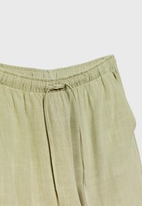 Light green elastic waistband pants with a drawstring, made of textured material. Features soft, flowing fabric with slight sheen.