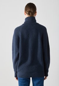 Pulover oversized, de culoare bleumarin, cu guler înalt, textură cu nervuri și umeri căzuți, realizat dintr-un material moale și confortabil.