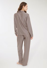 Donna in piedi a piedi nudi, di spalle, che indossa un top a maniche lunghe rigato verticale beige e nero abbinato e pantaloni larghi.