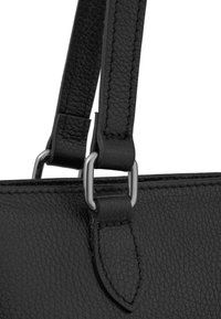 Sac à main en cuir noir texturé avec des détails cousus et un attachement en métal square argenté reliant la sangle au sac.