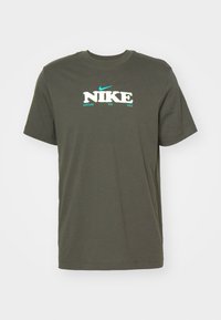 Olivengrøn bomulds t-shirt med korte ærmer, rund halsudskæring og et fedt "NIKE" logo i hvid og aqua, med "NURTURE THE SOLE" nedenfor.