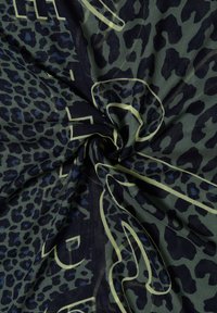 Tissu vert foncé avec imprimé léopard noir et bleu, torsadé, présentant des formes abstraites délimitées en jaune pâle et un texte partiel.