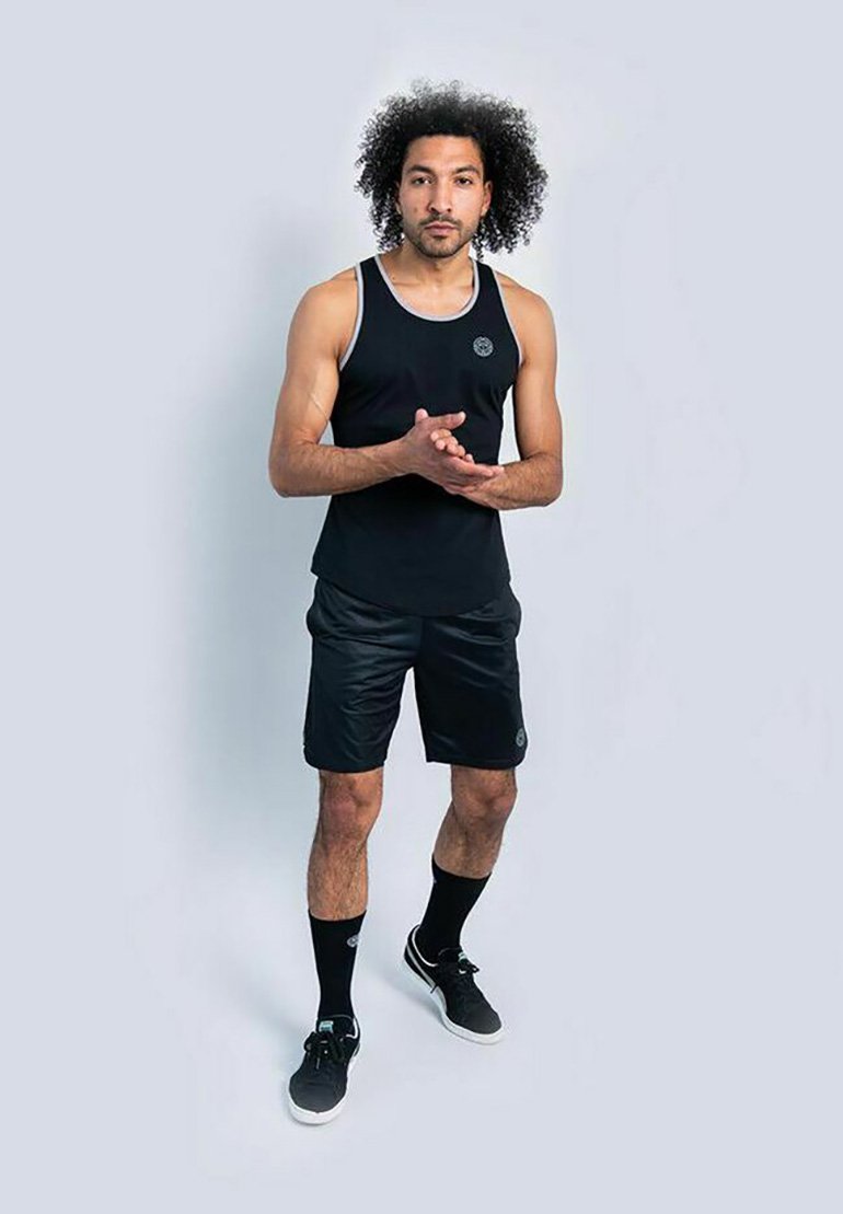 Canotta atletica nera e pantaloni corti realizzati in tessuto leggero, con un logo rotondo sul petto, abbinati a calzini neri e scarpe da ginnastica.