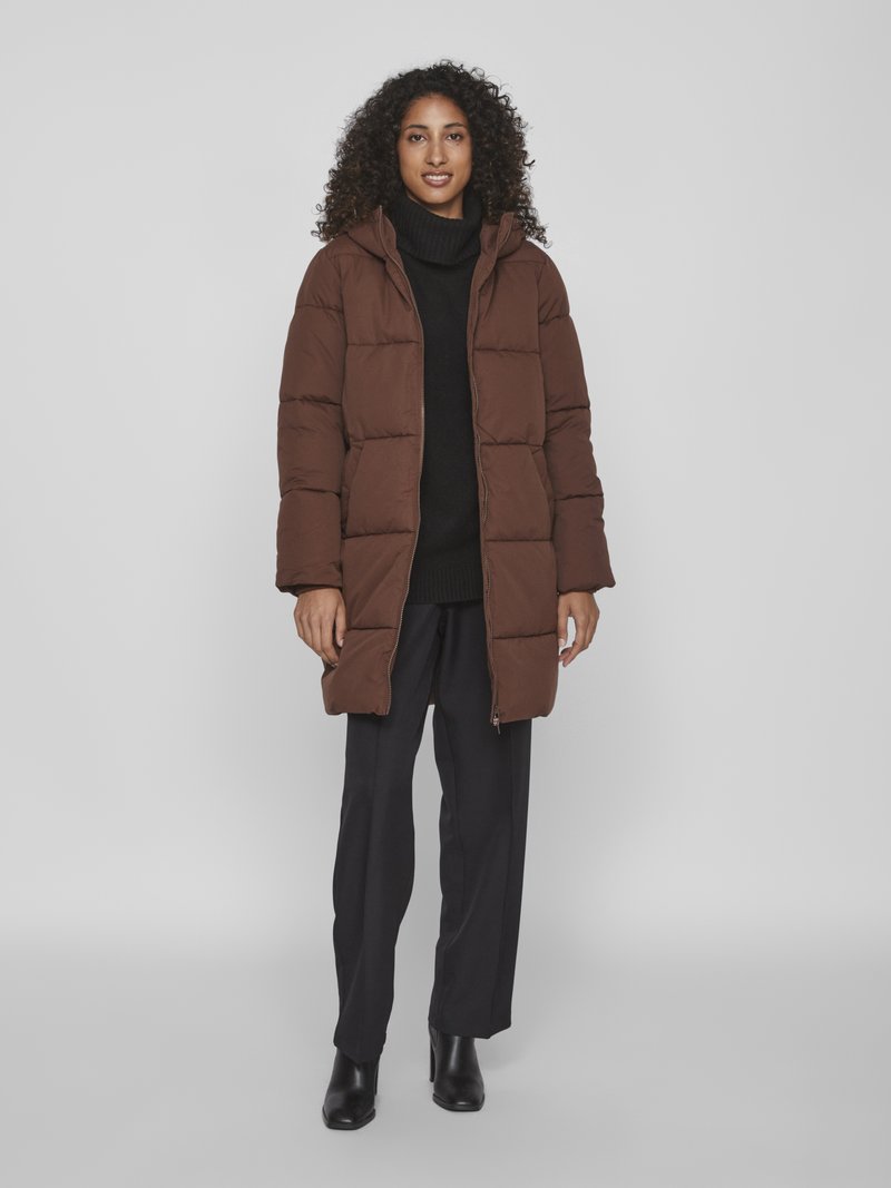 Brauner Puffermantel mit Kapuze, gep quiltetes Design und Reißverschluss, getragen über einem schwarzen Strickrollkragenpullover und schwarzen Hosen, kombiniert mit Absatzstiefeln.