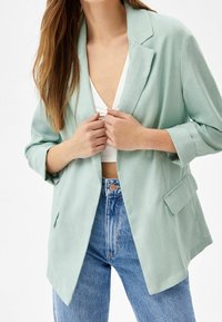 Blazer tissé vert clair avec un revers cranté, deux poches avant et des manches retroussées, associé à un jean en denim taille haute.