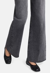Ballerines noires avec un bout rond, présentant une tige texturée et un capuchon de couleur contrastante. Associées à un jean large gris.