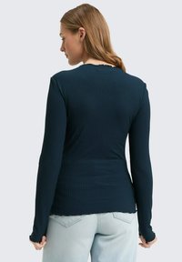 Navy-blaues langärmliges Oberteil mit einem dezenten gewellten Ausschnitt und zarten Rüschensäumen, kombiniert mit hellblauen Denim-Jeans.