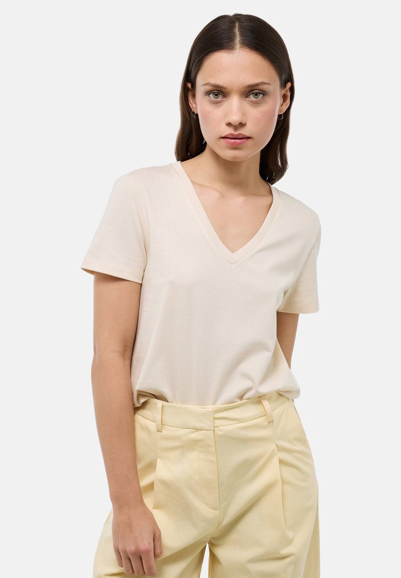 T-shirt beige en V en tissu doux avec des manches courtes, associé à un pantalon taille haute jaune clair avec des plis à l'avant.