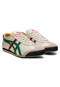 Baskets en cuir beige avec des bandes vertes et rouges, bouts noirs, semelles beiges et doublure intérieure jaune, présentées côte à côte sur un fond blanc.