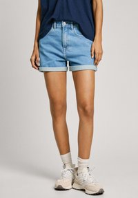 Ljusblå denimshorts med upprullade ärmar, femficksdesign och knappslutning fram. Bärs tillsammans med beige sneakers och vita strumpor.
