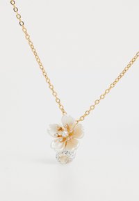 Collana in oro con un pendente a forma di fiore bianco, arricchita da perle e cristalli, insieme a un grande gemstone trasparente.
