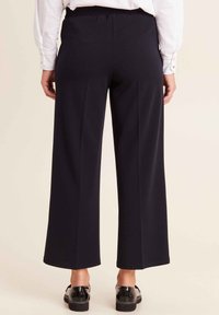 Zwarte wijde broek met een gladde textuur en een elastische tailleband, gecombineerd met glanzende zwarte schoenen. Eenvoudig ontwerp zonder zichtbare patronen.