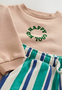 Beige Sweatshirt mit grünem, kreisförmigem "HAPPY COOL KID"-Text, kombiniert mit weißer, türkisfarbener und blauer vertikal gestreifter Hose mit elastischem Bund.