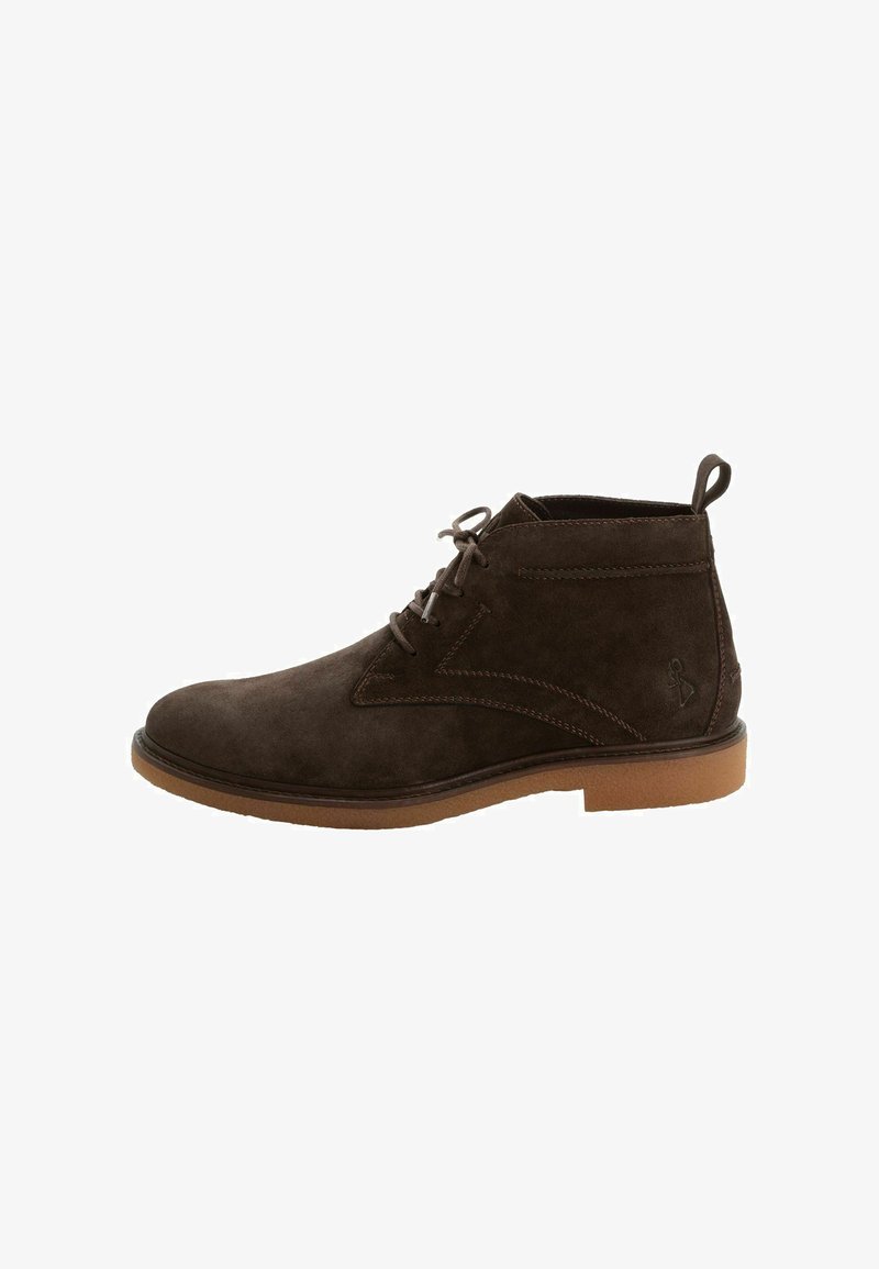 Bottine en daim marron foncé avec lacets à l’avant, languette au talon et semelle en caoutchouc marron clair.